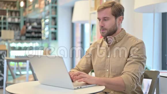 颈部疼痛的年轻人在咖啡厅使用笔记本电脑视频的预览图