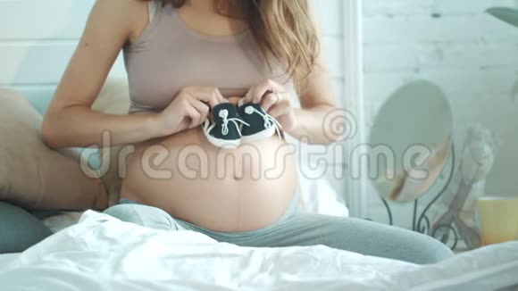 孕妇腹部大中段踩小婴儿鞋在床上视频的预览图