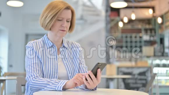 创意老女人在咖啡厅讲智能手机视频的预览图