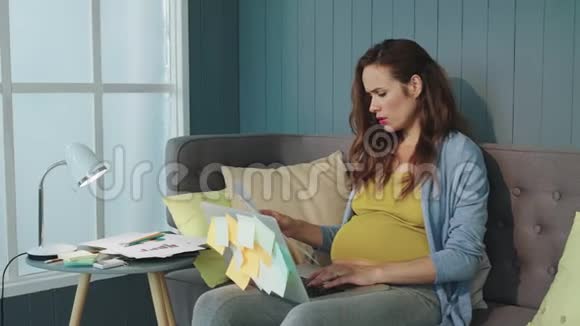 把注意力集中的怀孕女商人关在室内沙发上的笔记本电脑上视频的预览图