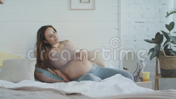 孕妇令人惊讶的婴儿在床上踢她的肚子肚皮妈妈抱着肚子视频的预览图