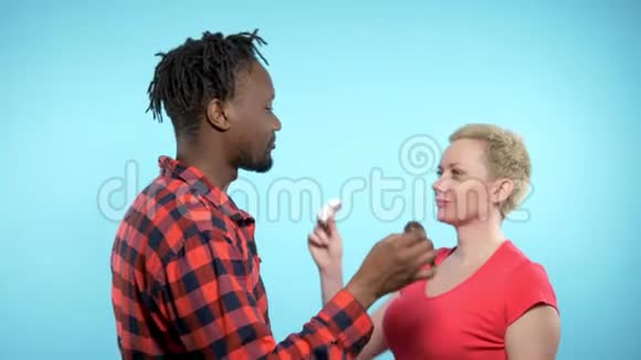 非洲男人白人女人吃黑白棉花糖蓝色背景视频的预览图