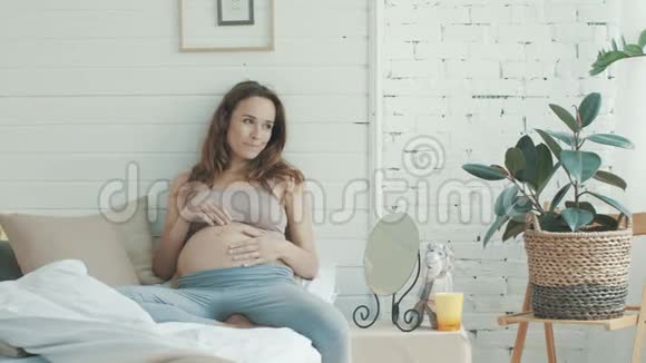美丽的孕妇在卧室摸肚子做梦的准妈妈视频的预览图
