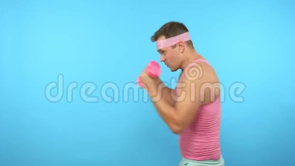 穿着粉红色衬衫的英俊男子正在与粉红色哑铃进行健身视频的预览图