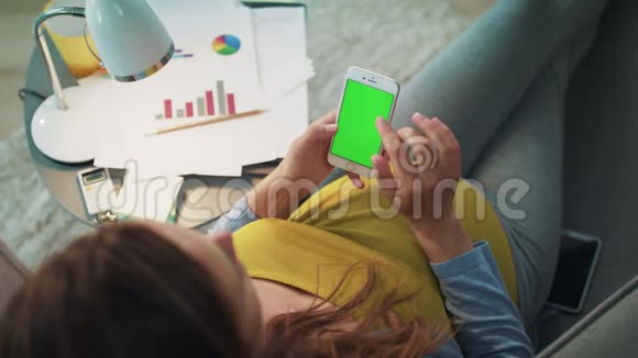 下班后贴身女商人用绿色屏幕智能手机放松视频的预览图