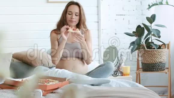 快乐的怀孕妈妈在床上吃披萨贝莉妈妈吃意大利菜视频的预览图