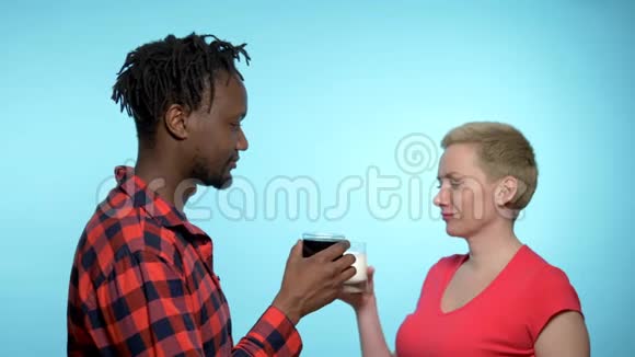非洲男人和高加索女人喝黑白鸡尾酒蓝色背景视频的预览图
