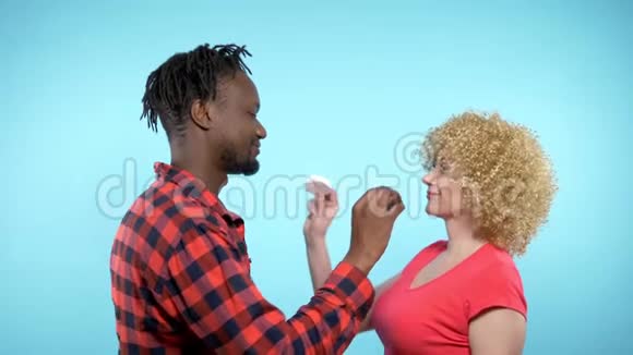 非洲男人白人女人吃黑白棉花糖蓝色背景视频的预览图