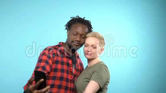 非洲男人和高加索女孩用智能手机自拍蓝色背景视频的预览图