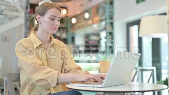 在咖啡馆里用手提电脑咳嗽的年轻女人视频的预览图