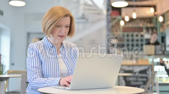 创意老女人在咖啡厅的笔记本电脑上庆祝视频的预览图