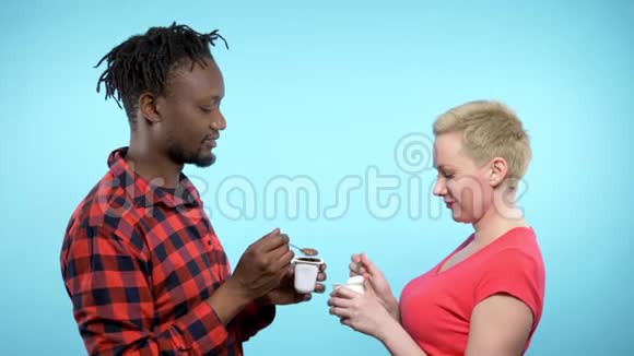 非洲男人白种人女人吃巧克力和奶油酸奶蓝色背景视频的预览图