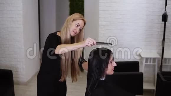 一位美丽的金发美发师用梳子缓慢地梳理着女性客户湿直发准备和准备视频的预览图