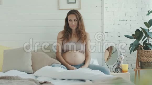 悲伤的孕妇坐在床上心烦意乱的准妈妈抱着枕头卧室视频的预览图