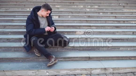 一个年轻人坐在楼梯上听音乐他摘下他的背包黑色耳机复制空间行动视频的预览图