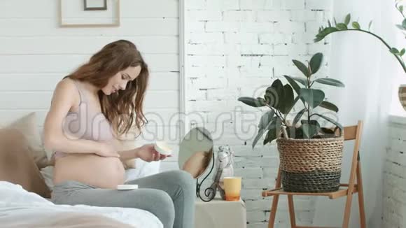 年轻孕妇在卧室的孕妇腹部涂护肤霜视频的预览图