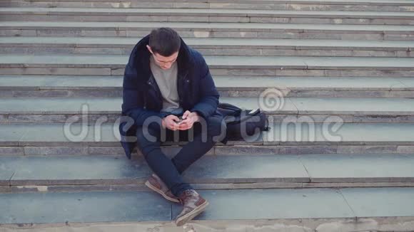 一个年轻人坐在楼梯上使用他的智能手机然后他就要把焦点放出来了复制空间行动视频的预览图