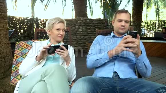 一对夫妇坐在户外咖啡馆里用智能手机视频的预览图