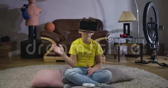 年轻的高加索儿童坐在VR耳机上移动他的手穿黄色T恤和蓝色牛仔裤的可爱卷发男孩视频的预览图