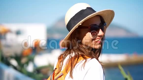 在阳光明媚的日子里穿着草帽和太阳镜在海边散步的迷人的慢动作微笑的女旅行者视频的预览图