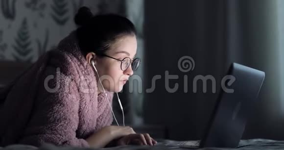 女人躺在床上带着笔记本电脑回家女学生戴着耳机在线学习网络教师学习语言视频的预览图