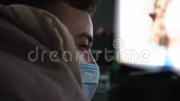 戴着医用面具的男性在家中观看有关冠状病毒的突发新闻视频的预览图