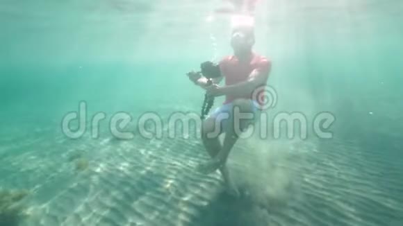 一名白人男子手持数码单反相机与三脚架拍摄水下视频的预览图
