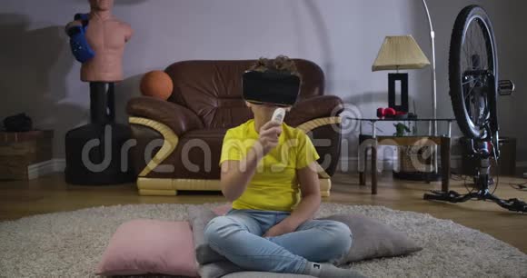 白人男孩在虚拟现实谷歌持有遥控器和弯曲穿黄色T恤和蓝色牛仔裤的男生视频的预览图