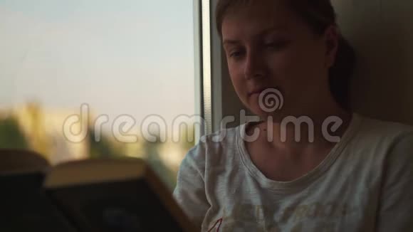 美丽的年轻的女孩在阳台上的公寓里在窗户边读一本书视频的预览图