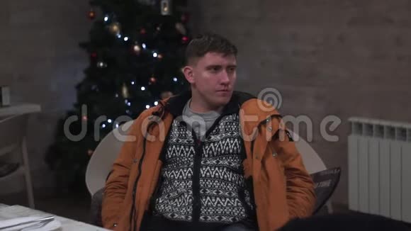穿着夹克的忧郁的家伙在圣诞树的背景下开派对视频的预览图