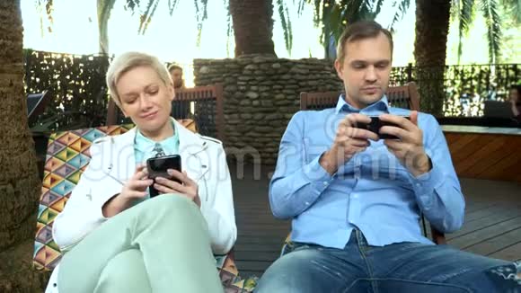 一对夫妇坐在户外咖啡馆里用智能手机视频的预览图