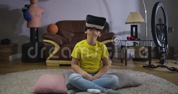 高加索男性青少年的特写坐在VR耳机上抬头微笑和交谈穿黄色T恤的可爱男孩视频的预览图