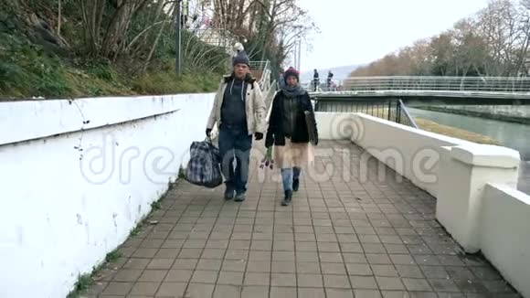 一对无家可归的男人和女人带着一只狗沿着河堤散步视频的预览图