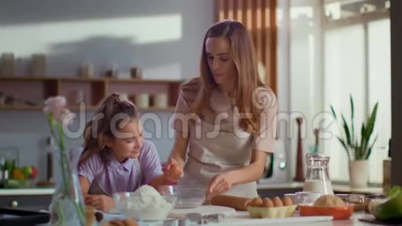 母亲和女儿在厨房玻璃碗里打碎鸡蛋的肖像视频的预览图