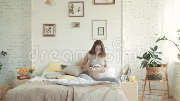 孕妇在腹部戴上耳机怀孕在床上听音乐视频的预览图