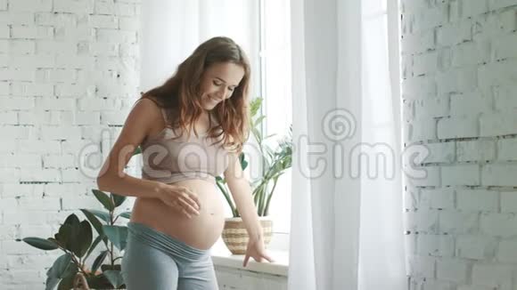特写孕妇摸肚子期待着妈妈站在家里的窗户上视频的预览图