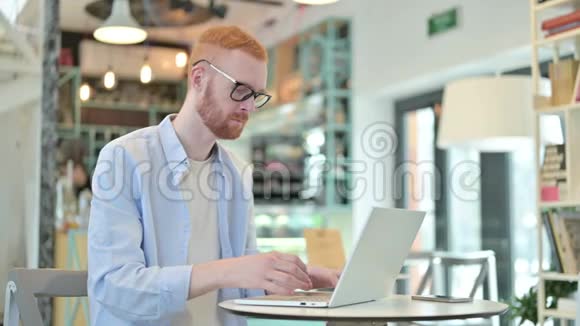 有笔记本电脑的红发男子在咖啡厅看镜头视频的预览图
