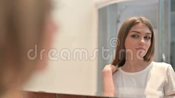 美丽的年轻女子镜中审视自己的后景视频的预览图