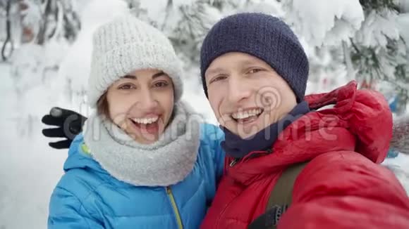 在寒冷的冬天年轻的一对夫妇在下雪的冬天公园散步男人和女人可爱地拥抱亲吻和欢笑视频的预览图