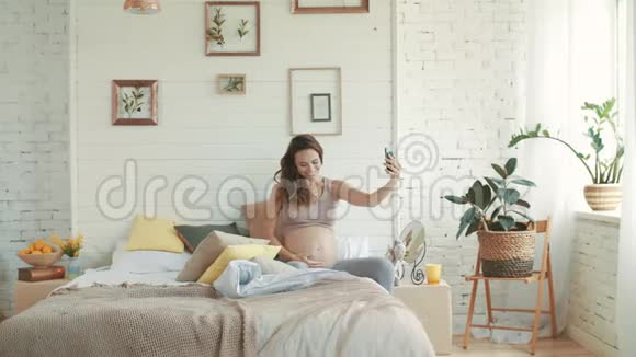 微笑孕妇自拍照片准妈妈坐在床上视频的预览图