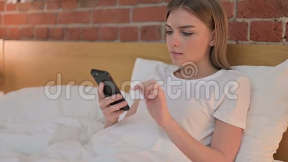 在床上使用智能电话失败的年轻女子视频的预览图