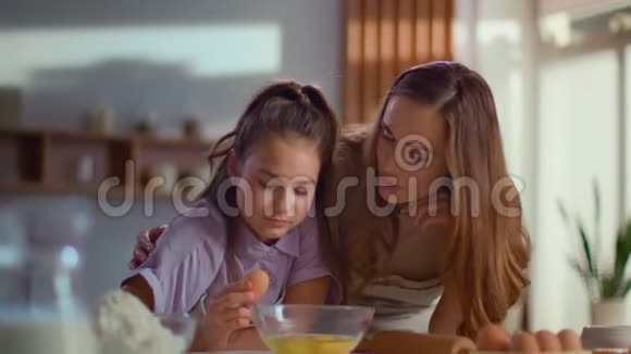 微笑的母亲和女儿把鸡蛋放进厨房的搅拌碗里视频的预览图