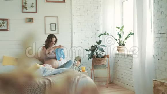 漂亮的孕妇在家看婴儿用品准妈妈坐在床上视频的预览图