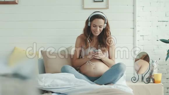 微笑孕妇在床上听音乐准妈妈在室内休息视频的预览图