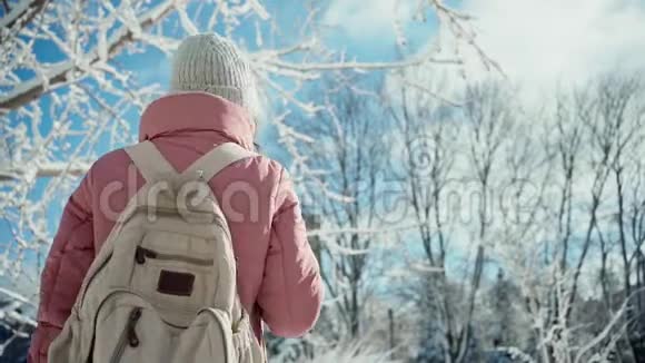 在温暖的粉红色公园里慢动作的年轻女子在白雪皑皑的冬日公园里散步视频的预览图