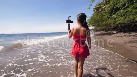 后视一位女性vlogger在海滩上散步和录制自拍视频视频的预览图