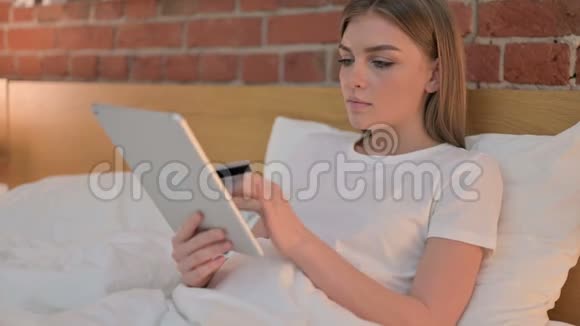 野心勃勃的年轻女子在床上平板电脑上获得在线支付成功视频的预览图