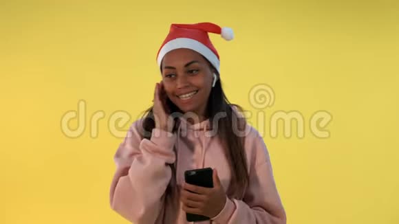 戴着圣诞帽和无线耳机听音乐的快乐非洲女人视频的预览图