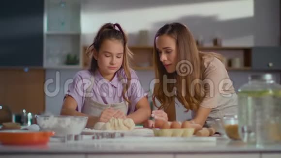 有魅力的女人教女孩在现代厨房为饼干准备面团视频的预览图