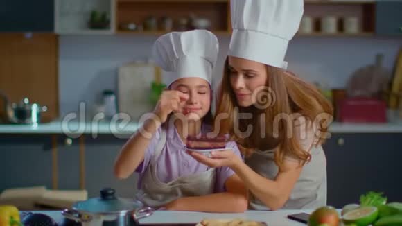 母亲和女儿戴着帽子在家庭厨房里用樱桃装饰蛋糕视频的预览图